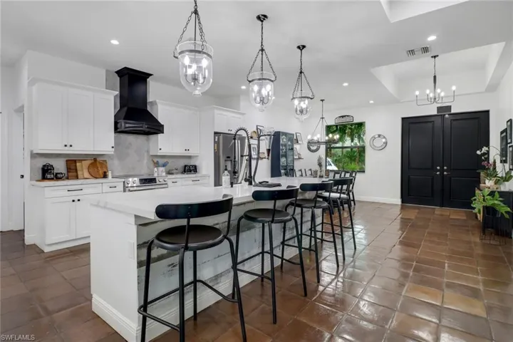 Kitchen featuring tasteful backsplash, stainless steel appliances, an island with sink, a raised ceiling, and custom range hood