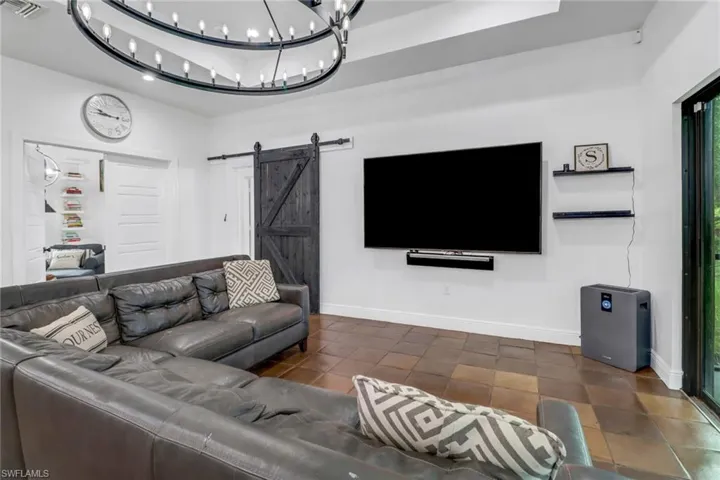 Living room featuring dark tile patterned flooring, a raised ceiling, a barn door, and an inviting chandelier