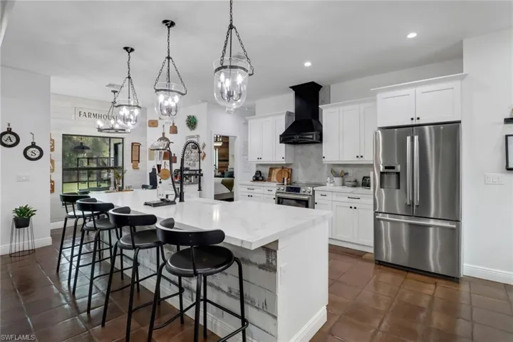 Kitchen featuring white cabinetry, premium range hood, an island with sink, appliances with stainless steel finishes, and a kitchen breakfast bar