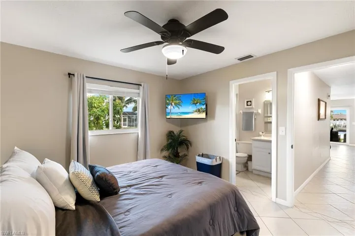 Bedroom with light tile patterned floors, ceiling fan, and ensuite bath