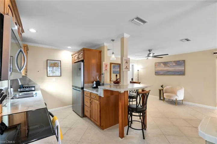 Kitchen with brown cabinets, appliances with stainless steel finishes, a kitchen bar, ornamental molding, and light tile patterned floors