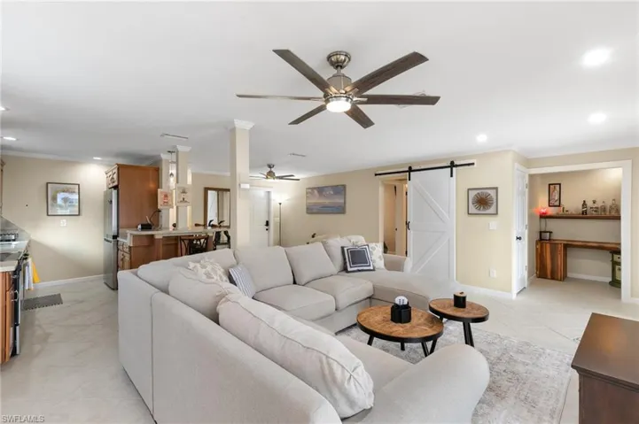 Living area with a barn door, recessed lighting, crown molding, ceiling fan, and light tile patterned flooring