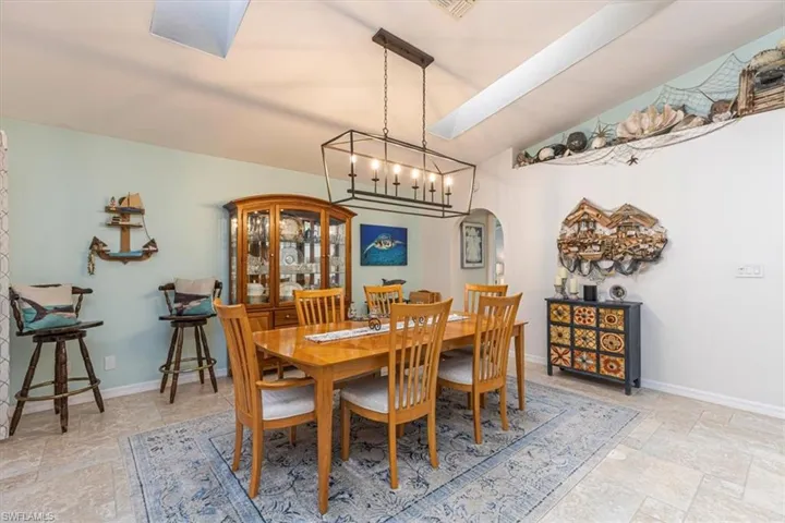 Dining room with stone tile flooring, a skylight, arched walkways, a chandelier, and vaulted ceiling