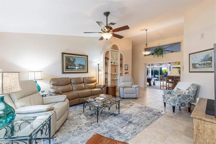 Living room featuring ceiling fan, vaulted ceiling, light stone finish flooring, and arched walkways