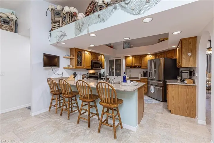 Kitchen featuring wood finish cabinetry, a breakfast bar, light stone countertops, open shelves, and a peninsula