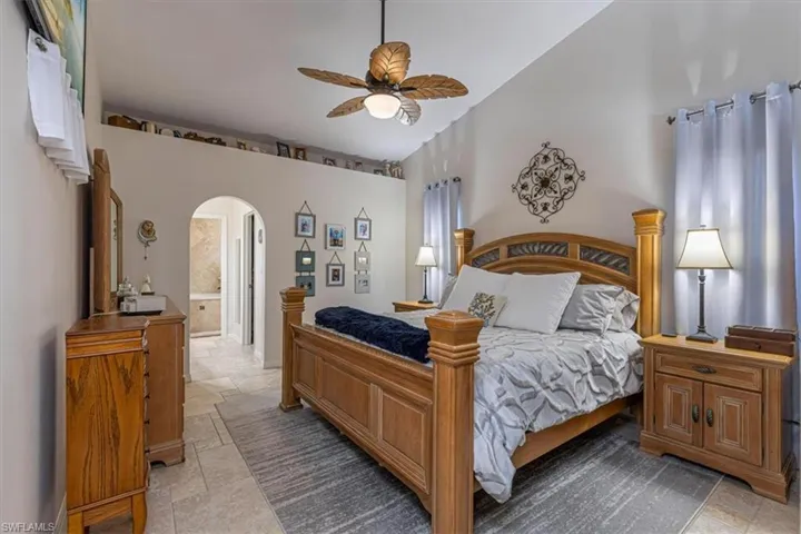 Bedroom featuring arched walkways, stone tile flooring, a ceiling fan, and lofted ceiling