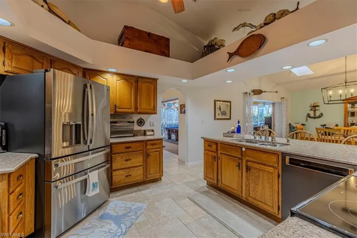 Kitchen featuring stainless steel appliances, wood finish cabinets, stone tile floors, a ceiling fan, and vaulted ceiling