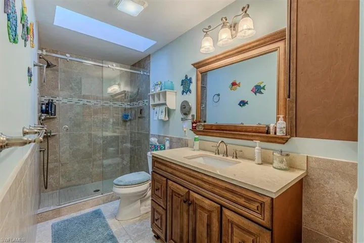 Full bath with vanity, a skylight, a stall shower, wainscoting, and tile walls