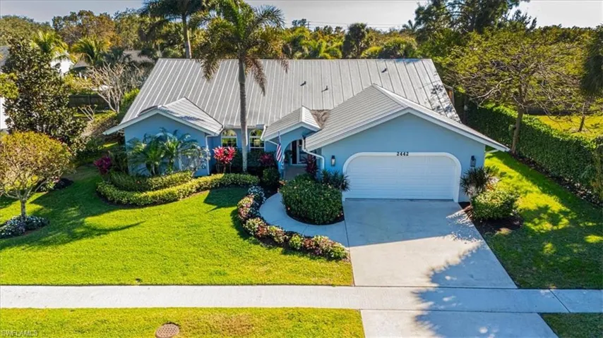 View of front facade with a front yard, a garage, concrete driveway, stucco siding, and a metal roof