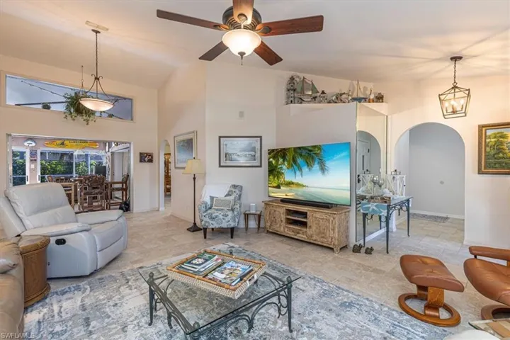 Living area featuring arched walkways, lofted ceiling, stone tile flooring, and ceiling fan