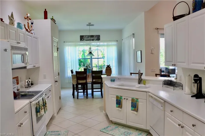 Kitchen with a sink, white cabinetry, light tile patterned floors, and white appliances