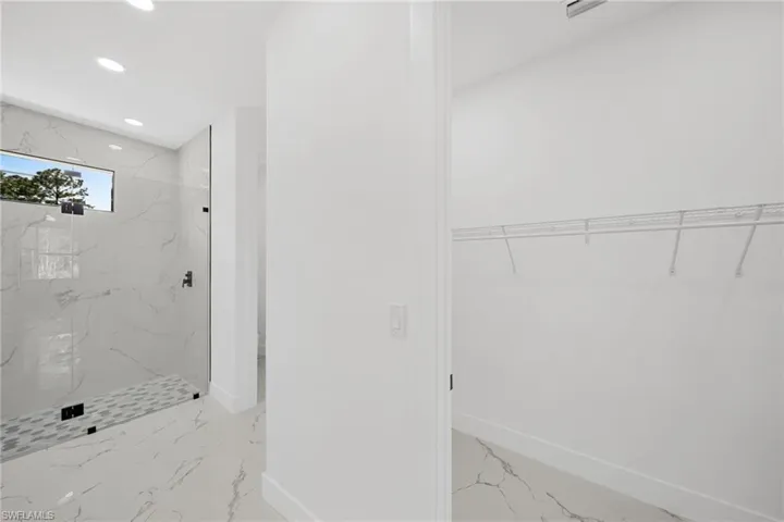 Full bath with a marble finish shower, a spacious closet, recessed lighting, and light marble finish flooring