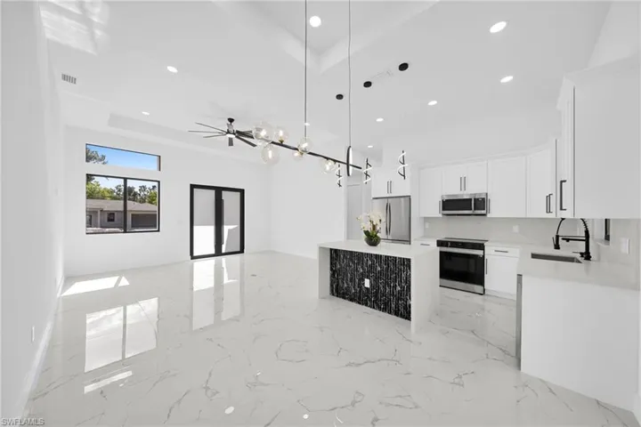 Kitchen with open floor plan, light stone countertops, white cabinetry, stainless steel appliances, and light marble finish floors
