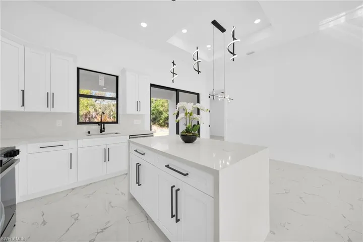 Kitchen with white cabinets, light marble finish flooring, a center island, stainless steel range oven, and a raised ceiling