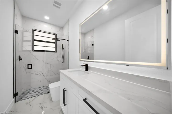 Bathroom with a marble finish shower, vanity, recessed lighting, and light marble finish floors