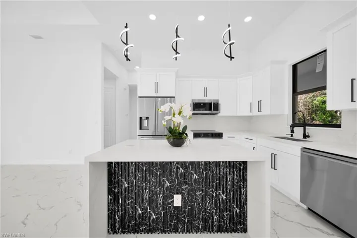 Kitchen featuring stainless steel appliances, light stone countertops, white cabinetry, and a kitchen island