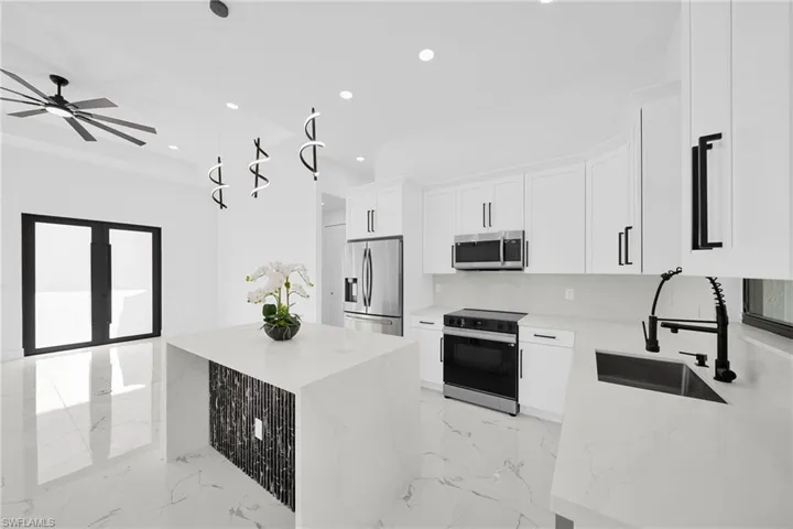 Kitchen featuring hanging light fixtures, stainless steel appliances, white cabinets, and light stone countertops