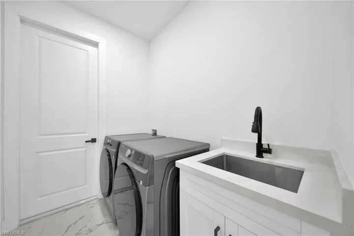 Laundry area featuring light marble finish flooring, washing machine and dryer, and cabinet space