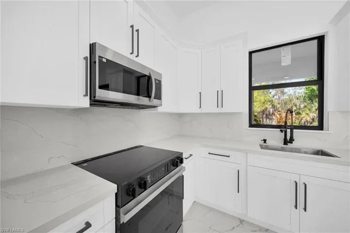 Kitchen featuring black electric range, stainless steel microwave, white cabinets, and light stone counters