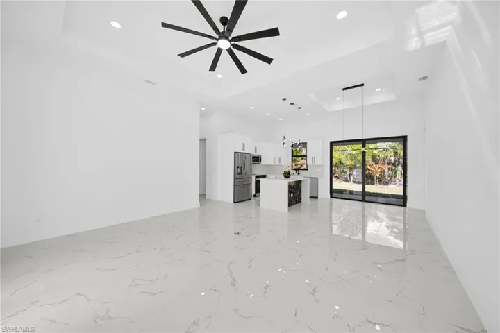 Unfurnished living room featuring recessed lighting, a ceiling fan, light marble finish flooring, and a high tray ceiling