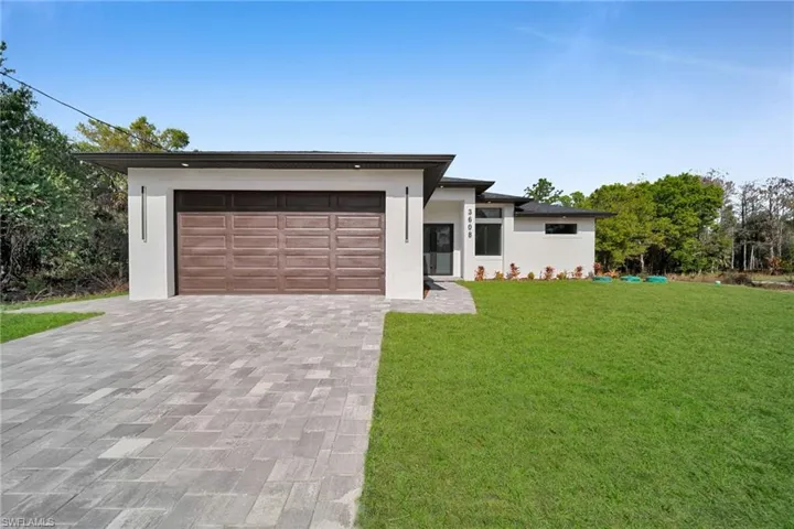 Prairie-style home featuring stucco siding, a front lawn, decorative driveway, and an attached garage