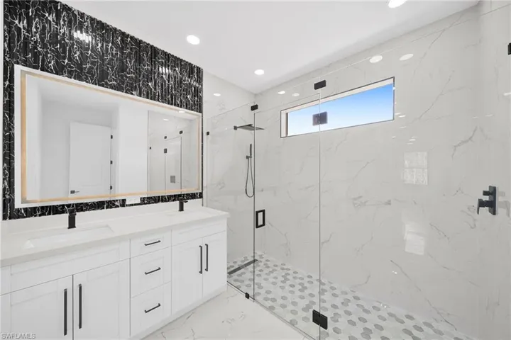 Full bath featuring a marble finish shower, double vanity, recessed lighting, and light marble finish floors