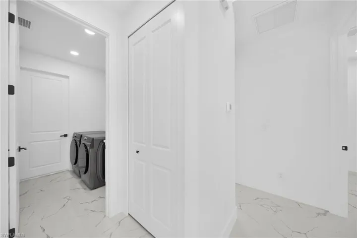 Laundry room featuring recessed lighting, light marble finish flooring, and washing machine and clothes dryer