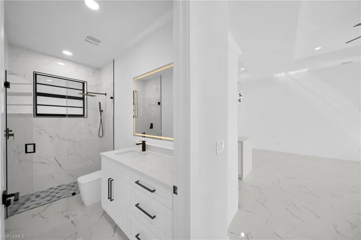 Bathroom with vanity, a marble finish shower, light marble finish flooring, and recessed lighting