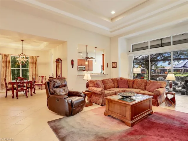 Living room with ceiling fan with notable chandelier, a raised ceiling, a high ceiling, and light tile patterned floors
