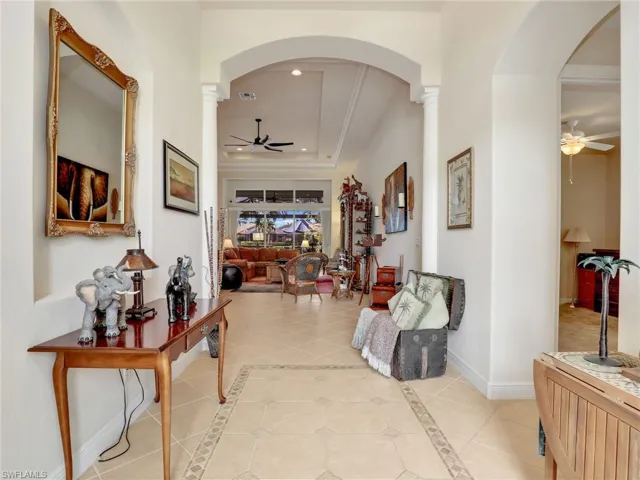 Hallway with light tile patterned floors, decorative columns, and a raised ceiling