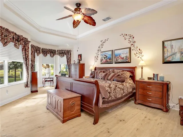 Bedroom with a raised ceiling, ornamental molding, ceiling fan, and light wood-type flooring