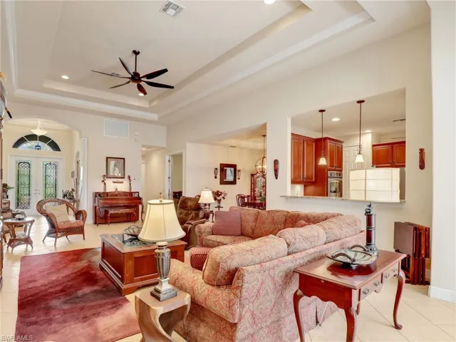 Living room featuring light tile patterned floors, a tray ceiling, ceiling fan with notable chandelier, and french doors