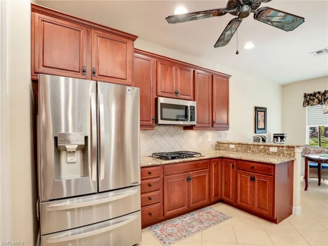 Kitchen with light stone counters, kitchen peninsula, ceiling fan, stainless steel appliances, and backsplash