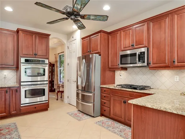 Kitchen featuring light stone counters, light tile patterned floors, ceiling fan, stainless steel appliances, and decorative backsplash