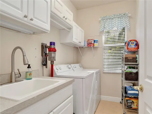 Laundry room featuring sink, light tile patterned floors, washing machine and dryer, and cabinets