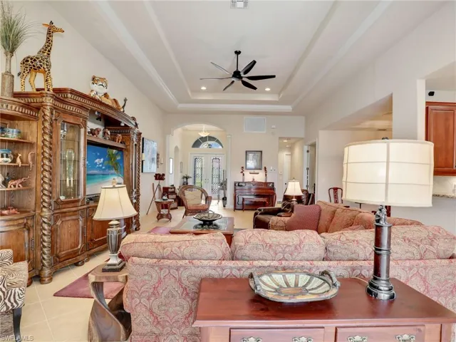 Tiled living room with a tray ceiling, french doors, and ceiling fan