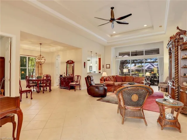 Tiled living room featuring a raised ceiling, ceiling fan with notable chandelier, and a high ceiling