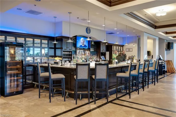 Community bar area featuring ornamental molding, hanging light fixtures, light stone counters, a high tray ceiling, and beverage cooler