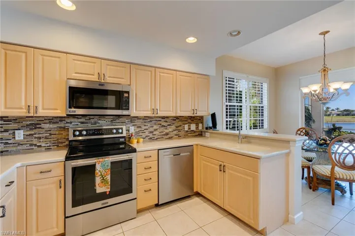 Kitchen featuring stainless steel appliances, light wood finish cabinets, light tile patterned floors, a peninsula, and hanging lights