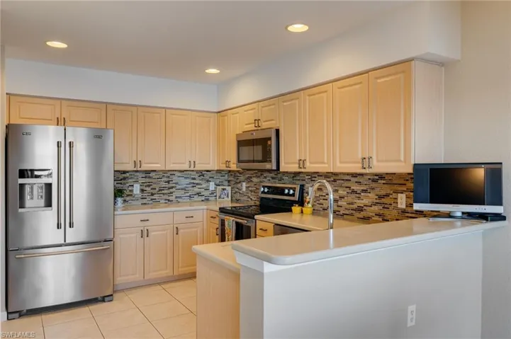 Kitchen with stainless steel appliances, light wood finish cabinets, light tile patterned floors, tasteful backsplash, and recessed lighting