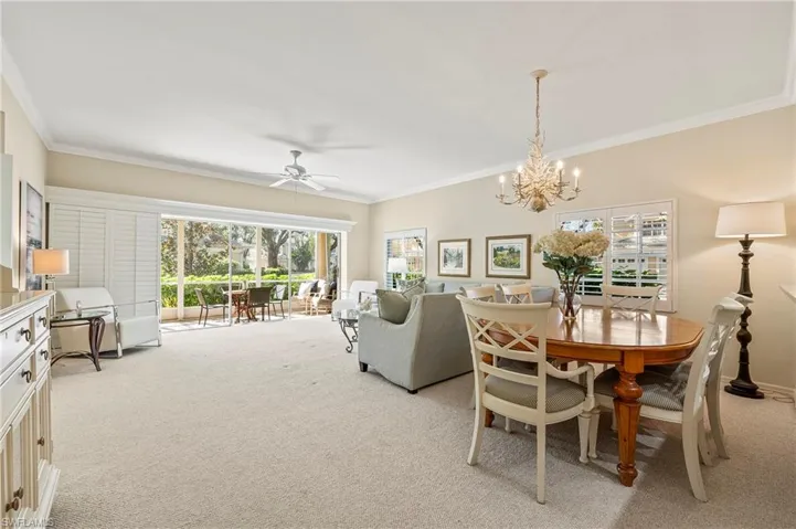 Carpeted dining area with ceiling fan with notable chandelier, crown molding, and a healthy amount of sunlight