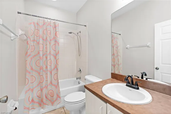 Bathroom featuring shower / bathtub combination with curtain, vanity, and light tile patterned floors