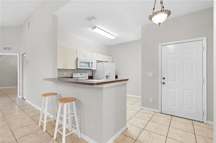 Kitchen featuring a kitchen bar, light tile patterned floors, a peninsula, white appliances, and decorative light fixtures
