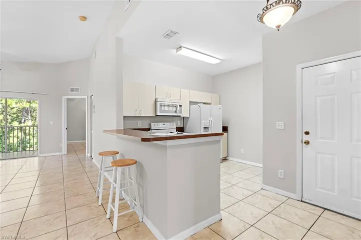 Kitchen featuring a kitchen breakfast bar, white appliances, a peninsula, and light tile patterned floors