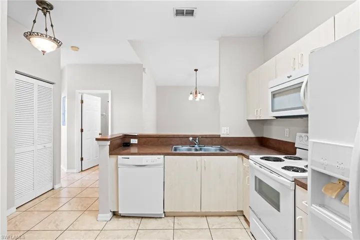 Kitchen featuring white appliances, decorative light fixtures, a peninsula, dark countertops, and light tile patterned floors