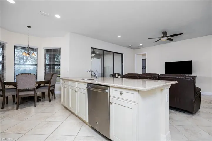 Kitchen with light stone countertops, stainless steel dishwasher, a ceiling fan, an island with sink, and open floor plan