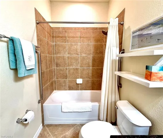 Bathroom featuring shower / tub combo with curtain, a textured wall, and tile patterned flooring
