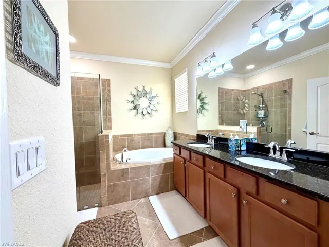 Full bath featuring a shower stall, double vanity, a garden tub, light tile patterned flooring, and crown molding