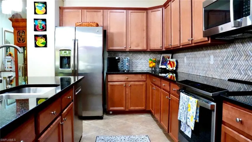 Kitchen featuring stainless steel appliances, brown cabinetry, dark stone counters, and light tile patterned flooring