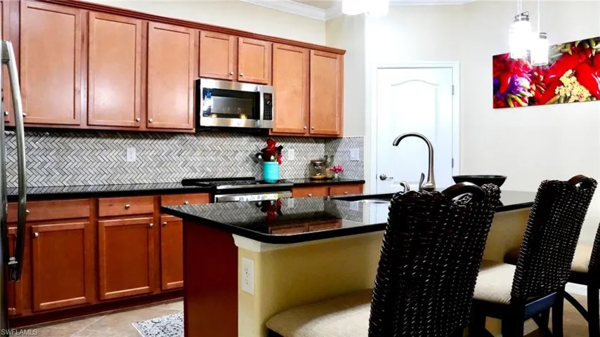 Kitchen featuring an island with sink, backsplash, appliances with stainless steel finishes, brown cabinets, and a kitchen breakfast bar